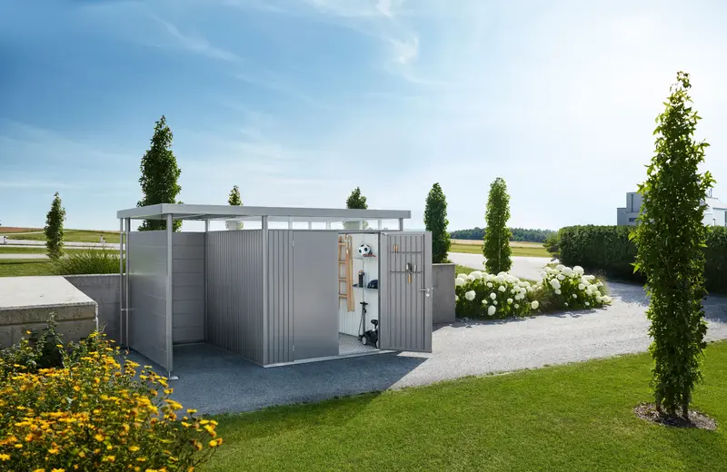 Metalno spremište Biohort HighLine s bočnom nadstrešnicom na šljunčanom prilazu uz vrt